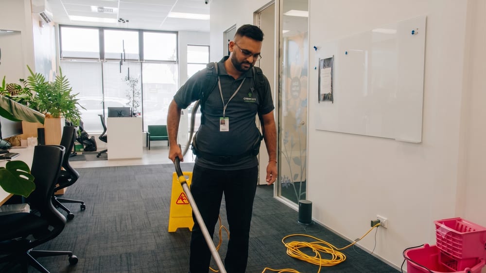 Crewcare cleaner vacuuming an office